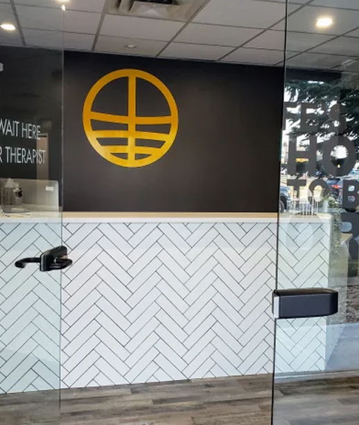 Modern office interior with a glass door, white herringbone tile wall, black upper wall featuring a large yellow circular geometric log